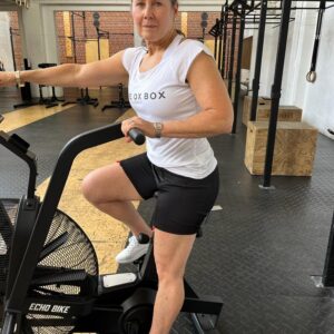 A woman in Britain hits the gym on a stationary bike, confidently prepared for her workout routine thanks to her EasyReach women's no-bend undergarments.