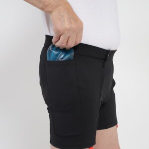 A figure carefully positions a blue ice pack inside a black therapeutic compression wrap, securing it around their thigh for targeted hip joint pain relief.