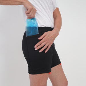 A person in a white t-shirt and black adaptive shorts demonstrates inserting an EasyReach cooling gel pad for the body into a specially designed pocket on the side of the shorts.