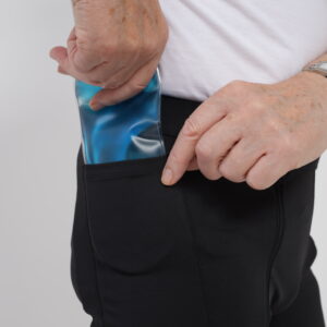 A person slides an EasyReach Cool Gel Inserts for Recovery into the side pocket of their black adaptive shorts.