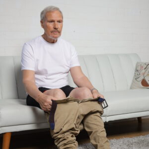 A man relaxes on a white sofa, showcasing EasyReach underwear – the perfect choice for those seeking the best no-bend undergarments in Britain – while holding a pair of trousers.